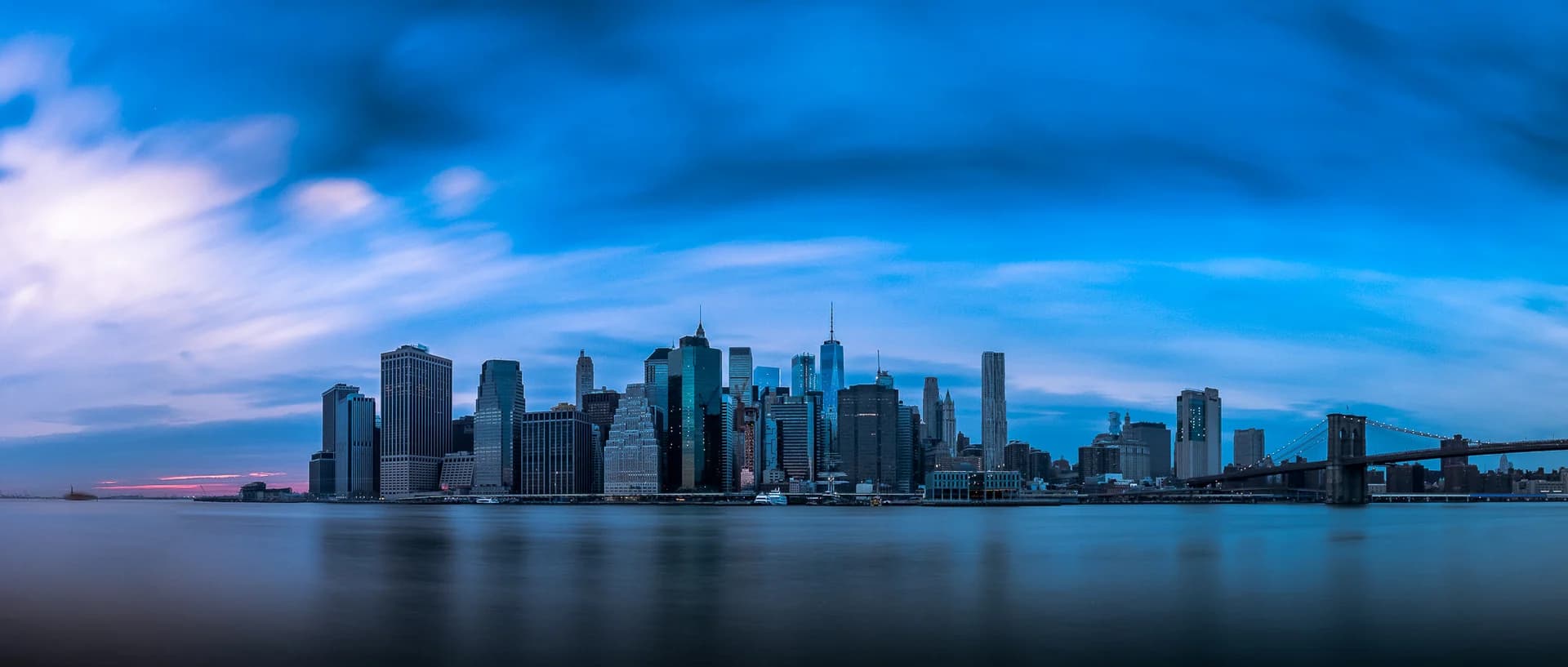 Manhattan skyline and Brooklyn Bridge across the East River at blue hour
